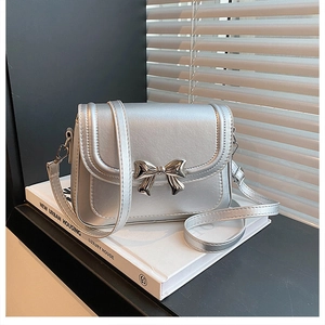 Détail d'un sac bandoulière argenté mat avec noeud métallique et coutures soignées