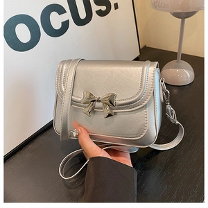 Détail d'un mini sac argenté avec boucle en forme de nœud métallique et texture en cuir