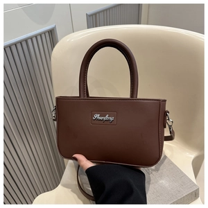 Detail of dark brown leather handbag featuring round handle and silver metal logo