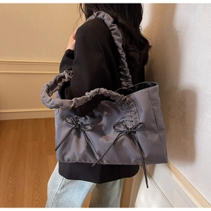Detail of grey tote bag featuring pleated shoulder straps and black ribbon bow accents