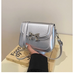 Détail d'un sac à main argenté métallisé doté d'un nœud décoratif en métal sur le rabat