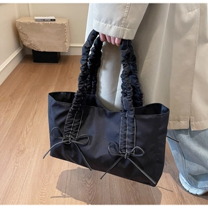 Detail of black tote bag with ruffled handles and bow accents for daily commuting