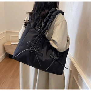 Detail of black tote bag with bow accents and pleated drawstring handle on a model