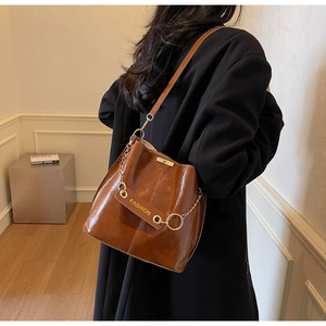 Brown leather bucket bag with gold chain and 'FASHION' tag worn by model in a room