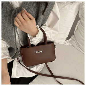 Detail of dark brown matte leather crossbody bag with metallic logo and strap