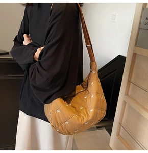 Detailed shot of brown quilted crescent bag with small white bow embroidery and wide strap