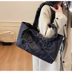 Detail showing the pleated ribbon straps and bow decorative accents on black nylon tote bag