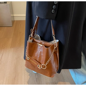 Detailed view of the brown leather bucket bag featuring a gold chain and metal hardware