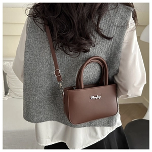 Brown PU leather handbag showing adjustable strap and double handles on a model