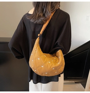 Detail of a brown quilted puffer crossbody bag with white bow patterns and adjustable strap
