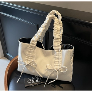 Detail of off-white puffer tote bag with ruffled handles and symmetrical ribbon bows