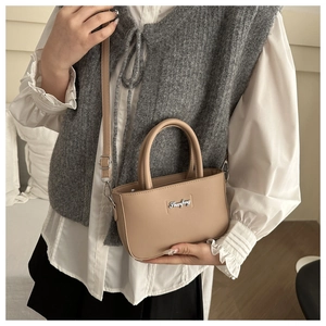 Detail view of beige crossbody bag with top handles and silver metal logo lettering