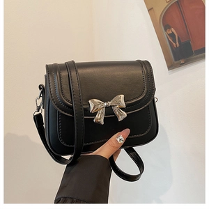 Détail d'un sac carré en cuir noir avec une boucle décorative en forme de nœud argenté