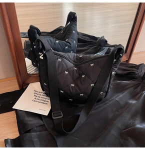 Detail view of a black quilted crescent bag with white bow embroidery and adjustable strap