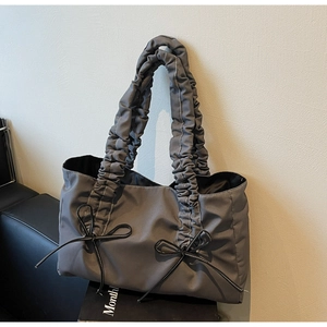 Detail view of a grey tote bag featuring pleated handles and decorative black bows