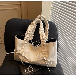 Detail of ruched strap and bow drawstring on cream tote bag placed on a sofa