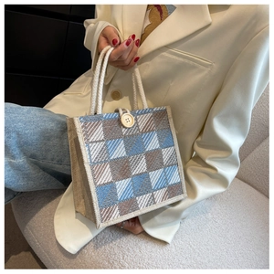 Detail of checkered woven linen handbag featuring blue patterns and white rope handle
