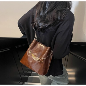 Detail of dark brown leather bucket bag with metal chain and fashion text engraving