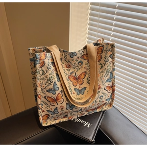 Detail view of a beige tote bag featuring blue and yellow floral butterfly embroidery