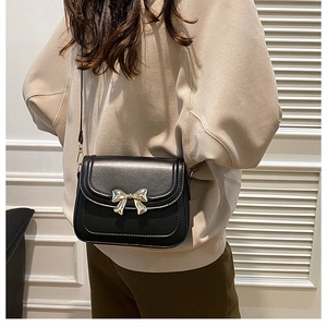 Détail du sac bandoulière noir avec un nœud en métal doré et fermeture à rabat chic