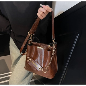 Detail view of dark brown leather bucket bag with gold chain and fashion hangtag
