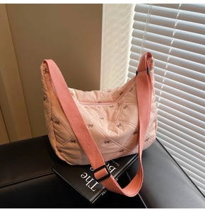 Detail of pink quilted dumpling bag featuring delicate bow embroidery and wide strap
