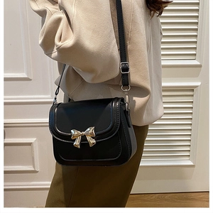 Mannequin portant un sac bandoulière noir en similicuir avec un nœud doré sur fond de porte