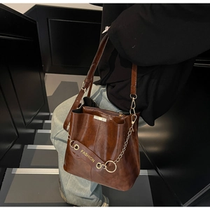 Detail of dark brown glossy leather bucket bag with chain strap and fashion pendant