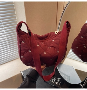 Detail view of quilted burgundy shoulder bag with white bow embroidery and mirror reflection