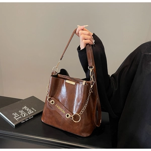 Close-up of brown leather bucket bag with gold chain and FASHION logo strap details