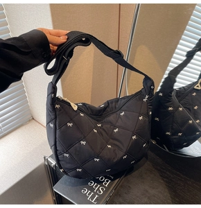 Detail of black quilted shoulder bag featuring white bow embroidery and wide fabric strap