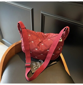 Detailed view of burgundy quilted shoulder bag with white bow embroidery and wide strap