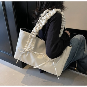 Detail of white tote bag featuring pleated ribbon handles and decorative bow accents