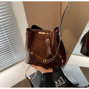 Detail view of brown patent leather bucket bag with gold chain strap and metal hardware