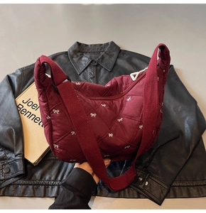 Detail of burgundy quilted nylon bag featuring embroidered white bow patterns and wide strap
