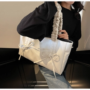 Close-up of white tote bag with pleated handles and decorative bows on nylon fabric