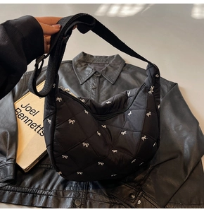Detail of black quilted shoulder bag featuring white bow embroidery and adjustable strap