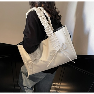 Chic cream tote bag with bow detail and ruched strap shown in an indoor staircase setting