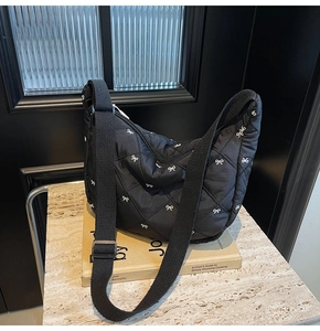 Detail of black quilted crescent bag with white bow embroidery and adjustable strap