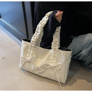 Close-up of a white textured tote bag featuring ribbon bows and pleated shoulder strap