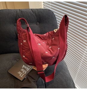 Detail of burgundy quilted tote bag with white bow embroidery on a cozy sofa setting