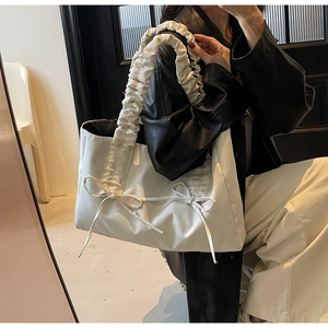 Detail of cream tote bag featuring ruffled handles and elegant bow decorations