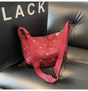 Close-up of diamond quilted burgundy crescent bag with white bow embroidery and wide strap