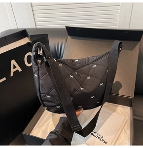 Detailed close-up of quilted black crossbody bag with white bow embroidery in gift box