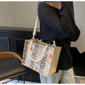 Ethnic woven tote bag with geometric patterns and white strap worn by a model