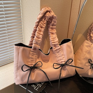 Pink nylon tote bag with pleated handle and black bow details in a soft lit room