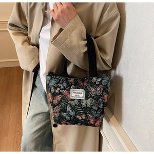 Detail of floral tote bag with colorful butterfly embroidery and black woven handle