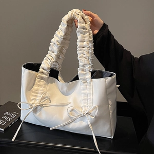White minimalist tote bag with ruffle handle and bow accents shown in model hand