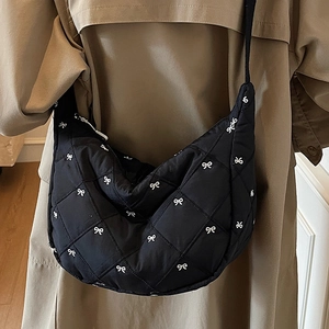 Quilted crescent crossbody bag in black with white bow patterns and zip closure
