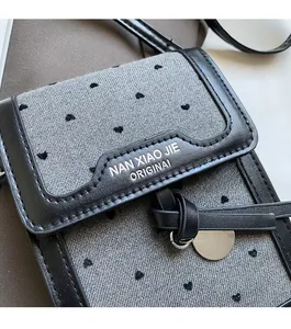 Détails d'un sac téléphone en denim à motif cœur avec finitions en cuir et charme